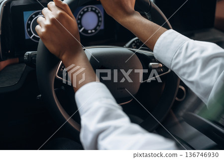 Two hands are on the steering wheel. Woman in white shirt is in the modern car Two hands are on the steering wheel. Woman in white shirt is in the modern car 136746930