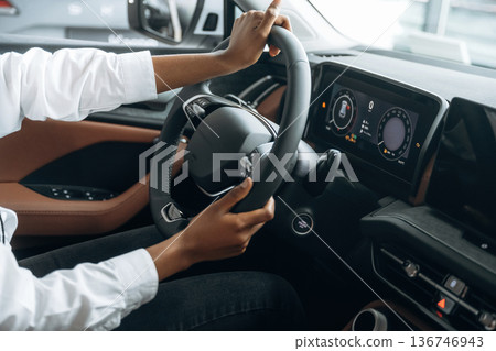 Control concept, hands on steering wheel. Woman in white shirt is in the modern car Control concept, hands on steering wheel. Woman in white shirt is in the modern car 136746943