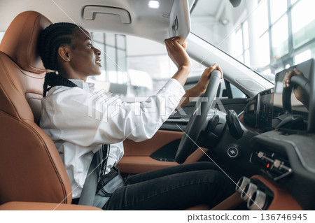 Looking in the mirror. Woman in white shirt is in the modern car Looking in the mirror. Woman in white shirt is in the modern car 136746945