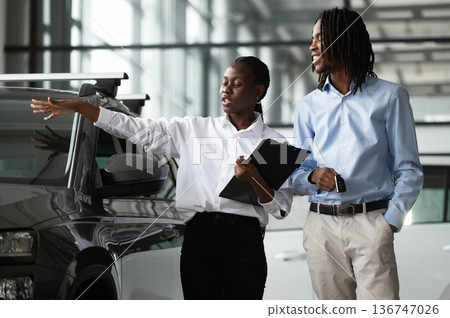 Explaining details. Car seller is assisting client in the automobile salon Explaining details. Car seller is assisting client in the automobile salon 136747026
