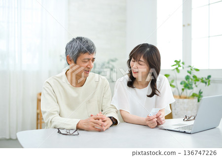 A couple in their 60s looking at a computer and cards in the living room 136747226