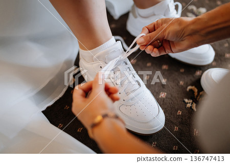 Bride getting ready tying white sneakers, modern wedding preparation moment 136747413