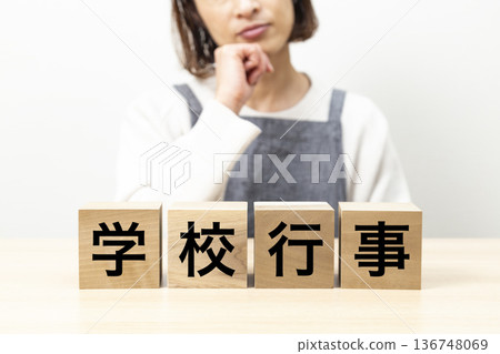 A block with the words "School Event" written on it and a woman wearing an apron A block with the words "School Event" written on it and a woman wearing an apron 136748069