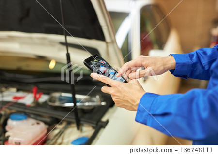 汽車修理工用智慧型手機拍攝引擎蓋內部的照片 汽車修理工用智慧型手機拍攝引擎蓋內部的照片 136748111