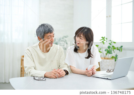 A couple in their 60s looking at a computer and cards in the living room A couple in their 60s looking at a computer and cards in the living room 136748175