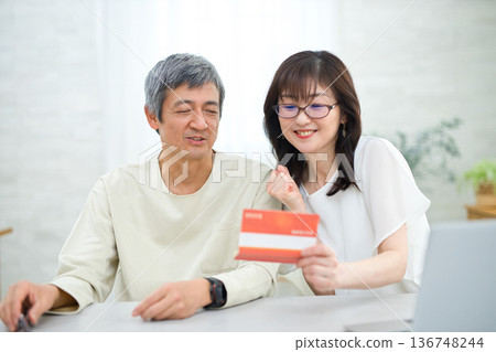 A couple in their 60s looking at their savings passbook in the living room 136748244