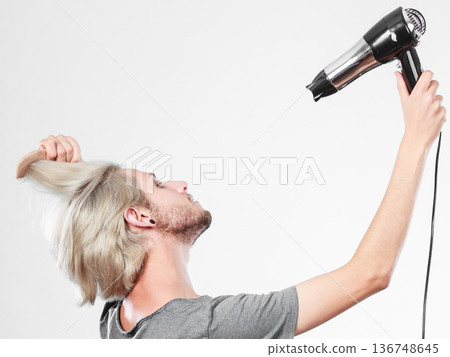 Young man drying hair with hairdryer Young man drying hair with hairdryer 136748645
