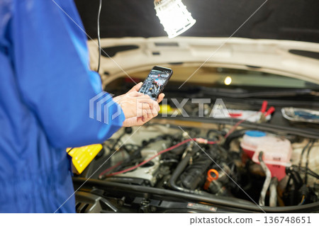 Auto mechanic taking a photo of the inside of the hood with a smartphone Auto mechanic taking a photo of the inside of the hood with a smartphone 136748651