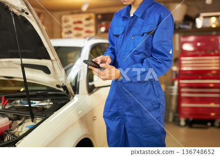 Auto mechanic taking a photo of the inside of the hood with a smartphone 136748652
