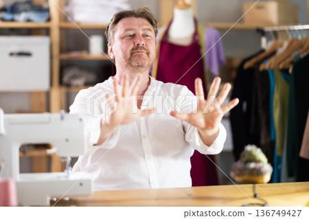Middle-aged male tailor stretching while sitting next to sewing machine 136749427