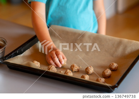 Children's hands make nut cookies and place them on a baking sheet Children's hands make nut cookies and place them on a baking sheet 136749738