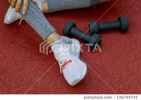 A girl rests on the sports ground after exercising with dumbbells 136749745