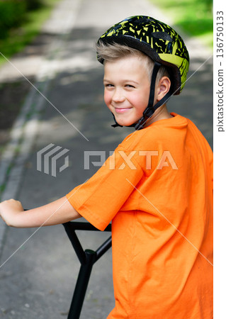 A young boy with blond hair and an orange T-shirt on a scooter A young boy with blond hair and an orange T-shirt on a scooter 136750133
