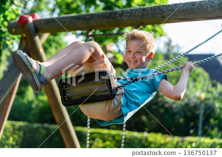 A boy in a blue T-shirt rides on a swing and smiles A boy in a blue T-shirt rides on a swing and smiles 136750137