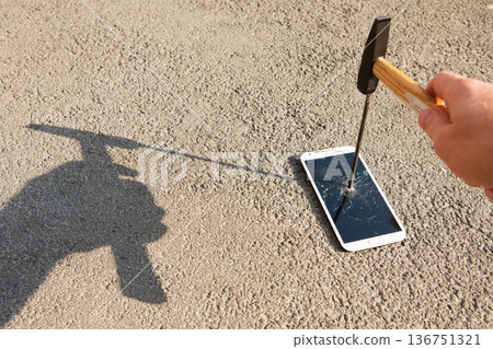 A hand drives a large metal nail through a smartphone screen with a hammer A hand drives a large metal nail through a smartphone screen with a hammer 136751321