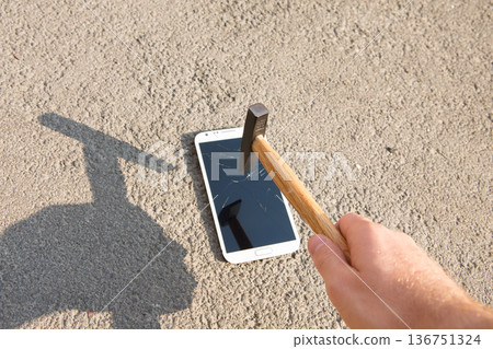 A hand drives a large metal nail through a smartphone screen with a hammer 136751324