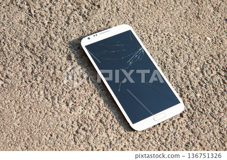 White smartphone with a severely cracked and shattered glass screen lying on rough outdoor asphalt 136751326