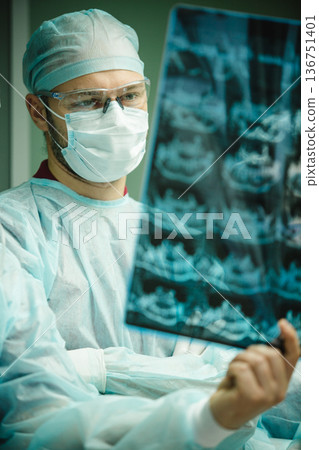 A focused male surgeon in sterile scrubs meticulously examines a dental X-ray 136751401