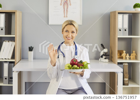 Smiling doctor with fresh vegetables waving, promoting healthy diet and nutrition Smiling doctor with fresh vegetables waving, promoting healthy diet and nutrition 136751957