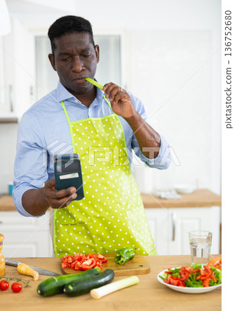 man using phone while preparing vegetable salad for dinner man using phone while preparing vegetable salad for dinner 136752680