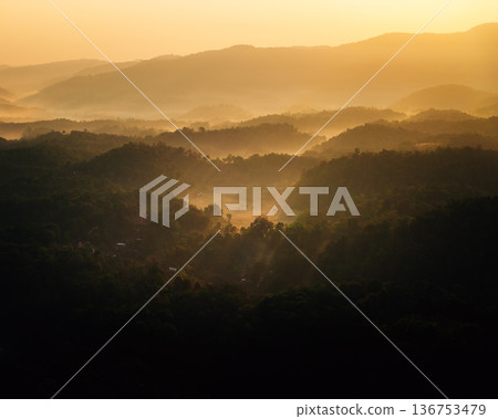 Aerial view of tropical mountain range covered in morning mist and golden sunlight Aerial view of tropical mountain range covered in morning mist and golden sunlight 136753479