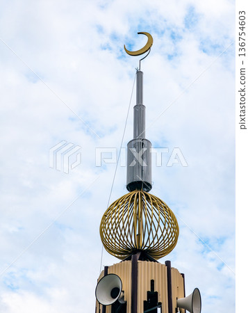 Islamic mosque minaret tower with golden crescent moon symbol and loudspeakers under blue sky and white clouds, religious architecture concept. 136754603