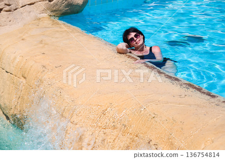 A woman swims in a pool with a waterfall 136754814