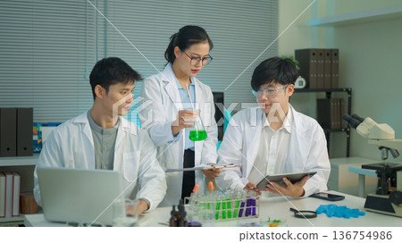 Research team discusses results while a scientist presents a green liquid sample, showing collaboration and analysis in a modern laboratory. Research team discusses results while a scientist presents a green liquid sample, showing collaboration and analysis in a modern laboratory. 136754986