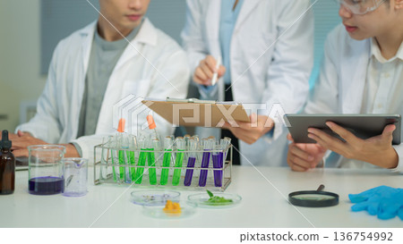 Cropped shot research team in lab coats analyzing test samples and recording data with laptop and tablet 136754992