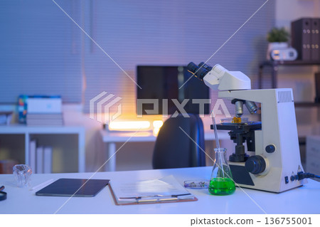 Laboratory workspace with microscope, green chemical solution, and research documents, representing modern scientific analysis and controlled experimentation. 136755001
