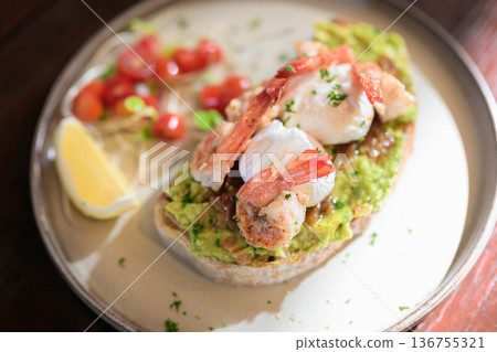 Open-faced toast topped with guacamole, shrimp, and poached eggs served with lemon and fresh garnish 136755321