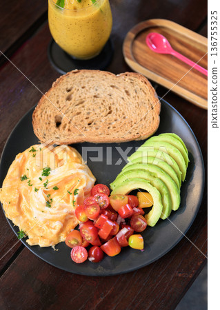 Balanced breakfast plate with eggs, sliced avocado, cherry tomatoes, toast, and a fruit smoothie 136755325