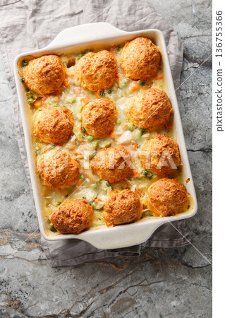 Chicken and biscuit casserole with added vegetables such as onions, carrots, green peas, celery with creamy sauce close-up in a baking dish. Vertical top view 136755366