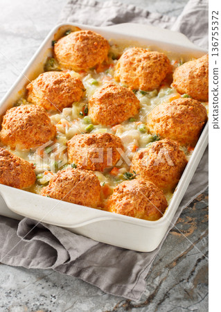 Chicken and Biscuit Casserole with frozen veggies, chicken broth, soup, and milk closeup on the baking dish. Vertical 136755372
