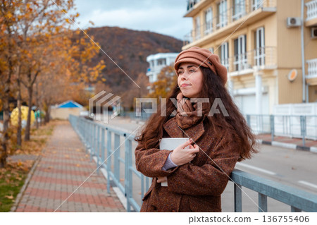 Warm drink and fresh air - stylish woman in a beret holds coffee during a solo walk. Calm, reflective moment in the heart of the city. Warm drink and fresh air - stylish woman in a beret holds coffee during a solo walk. Calm, reflective moment in the heart of the city. 136755406