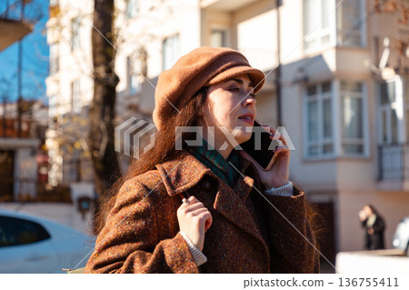 Portrait of a Caucasian young woman wearing coat and beret, calling on a smartphone on the street. City lifestyle 136755411