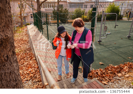 Elderly Caucasian woman strolling with granddaughter during afternoon park visit. Concept of active retirement and family wellbeing. Elderly Caucasian woman strolling with granddaughter during afternoon park visit. Concept of active retirement and family wellbeing. 136755444