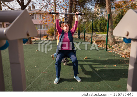 Elderly Caucasian woman training on a street gym in an urban park. Sport, wellness, and active senior lifestyle concept. Elderly Caucasian woman training on a street gym in an urban park. Sport, wellness, and active senior lifestyle concept. 136755445