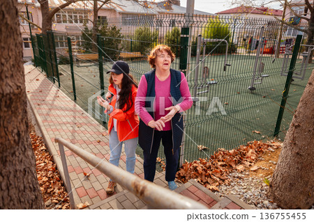 Mature grandmother walking hand in hand with her granddaughter in a sunny park. Outdoor enjoyment and senior lifestyle. 136755455