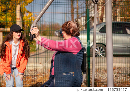 Mature woman trains with professional guidance on outdoor gym equipment. Recovery, mobility, and wellness in retirement. 136755457