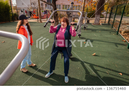Older woman exercises under supervision of a trainer as part of post illness recovery. Structured sport routine supports prevention and healthy aging. Older woman exercises under supervision of a trainer as part of post illness recovery. Structured sport routine supports prevention and healthy aging. 136755460