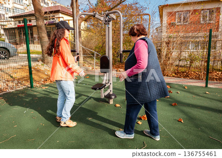 Senior Caucasian woman exercises outdoors with a fitness trainer during recovery after illness. Sport supports rehabilitation, strength, and active aging. Senior Caucasian woman exercises outdoors with a fitness trainer during recovery after illness. Sport supports rehabilitation, strength, and active aging. 136755461