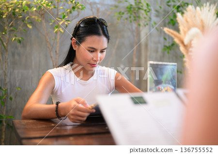 Woman Reading Menu at Outdoor Cafe with Tropical Plants Woman Reading Menu at Outdoor Cafe with Tropical Plants 136755552