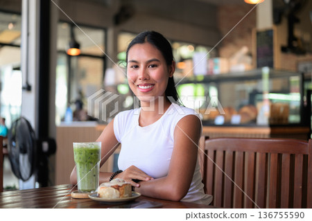 Smiling Woman Drinking Iced Matcha Latte at Cafe with Dessert 136755590