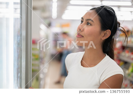 Smiling Woman Choosing Drink from Refrigerator in Supermarket 136755593