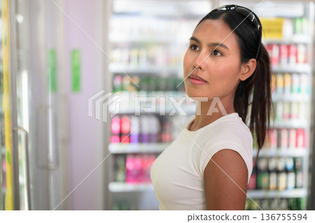 Smiling Woman Choosing Drink from Refrigerator in Supermarket 136755594