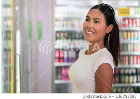 Smiling Woman Choosing Drink from Refrigerator in Supermarket 136755595