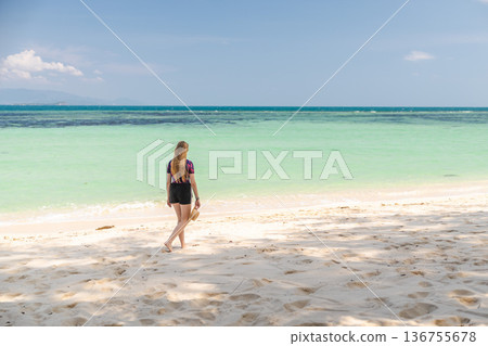 Young woman walking barefoot along sandy beach in Koh Samui, Thailand, holding hat and looking at turquoise sea under clear sky during summer travel Young woman walking barefoot along sandy beach in Koh Samui, Thailand, holding hat and looking at turquoise sea under clear sky during summer travel 136755678