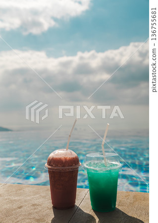 Two colorful cold drinks on infinity pool edge with ocean horizon and soft sky creating summer refreshment scene with wide copy space for travel and resort concepts 136755681