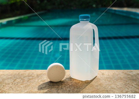 Pool chemical container and chlorine tablet on swimming pool edge with turquoise water background, pool sanitation and maintenance concept  136755682